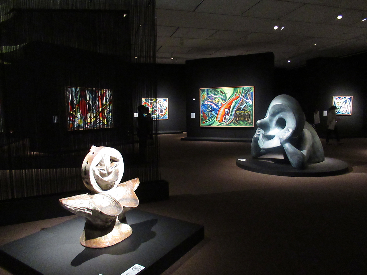 「展覧会　岡本太郎」展示風景　手前の立体は「顔」1952年、右は「若い夢」1974年、中央の絵画の大作は「森の掟」1950年
